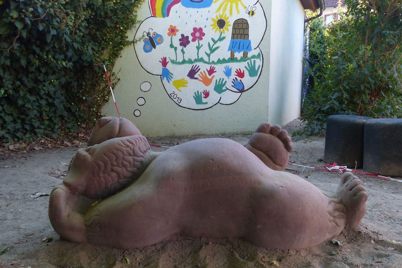 Steinskulptur liegende Bär im Sandkasten